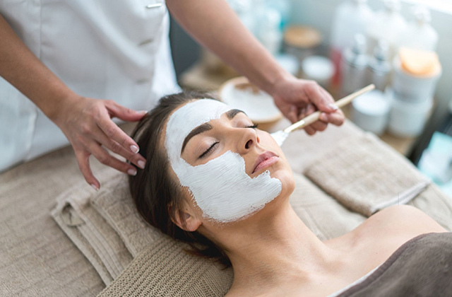 Masseue is applying face pack by a brush to lady face 